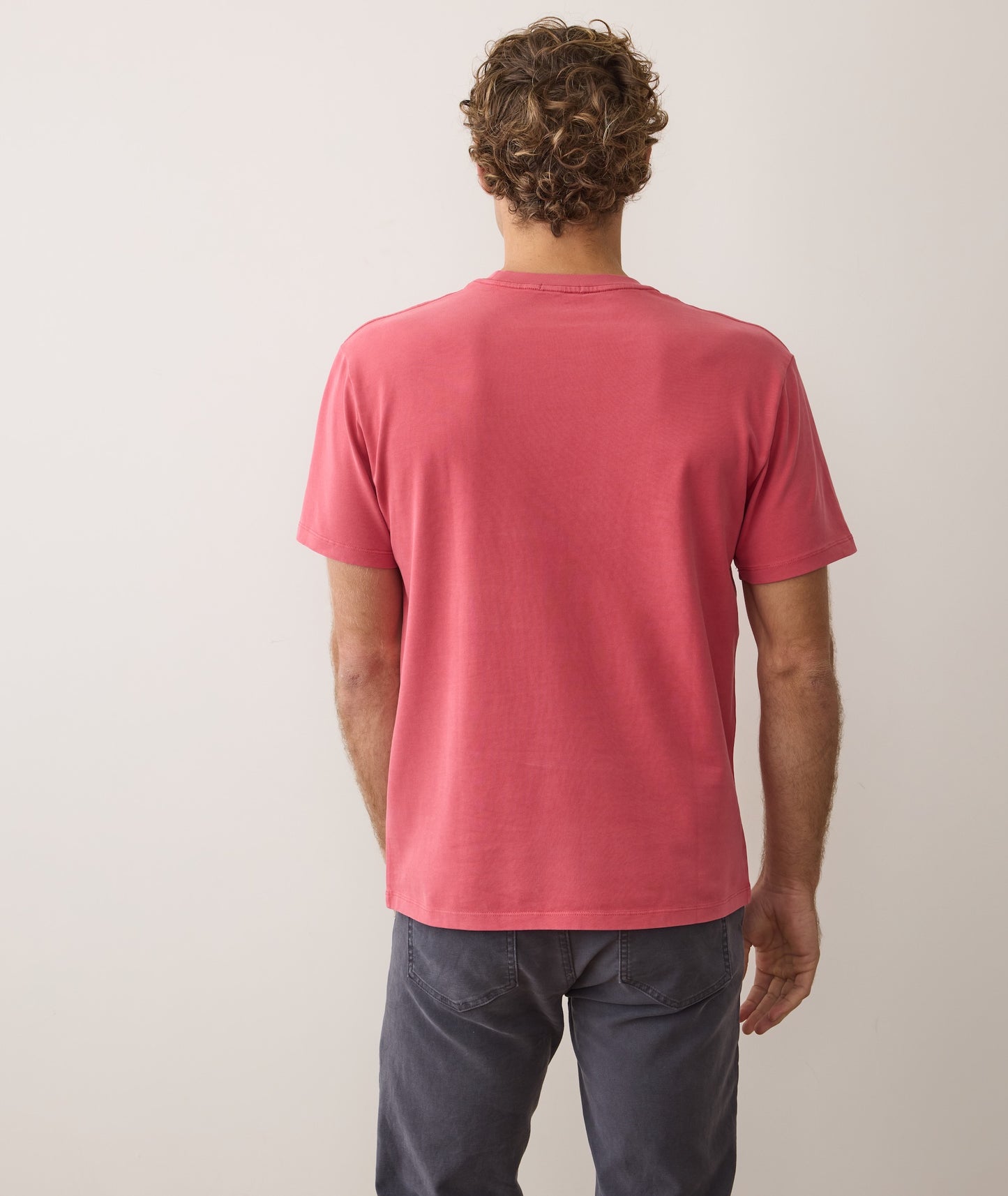 Man wearing a red t-shirt and dark pants against a plain background
