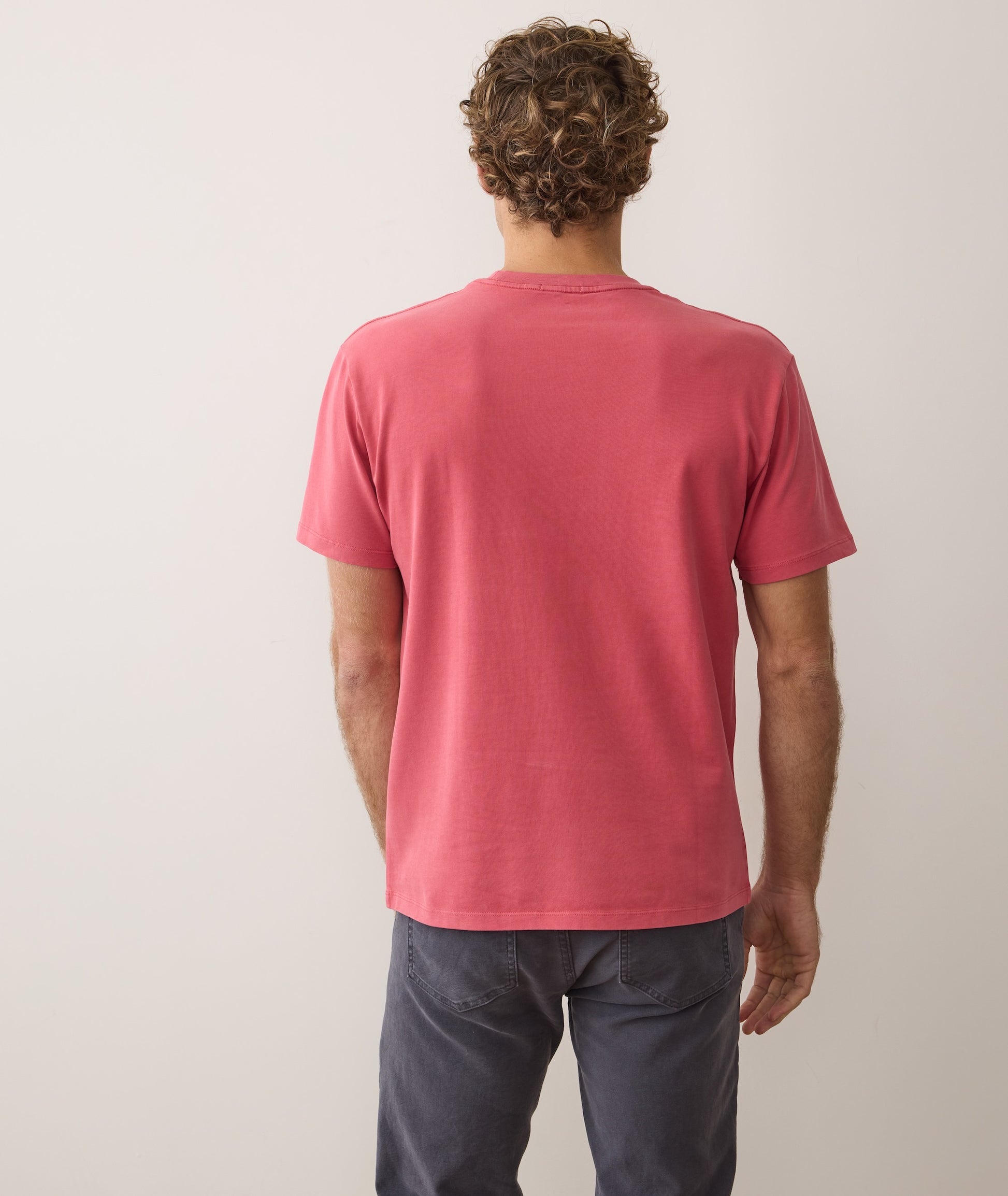 Man wearing a red t-shirt and dark pants against a plain background