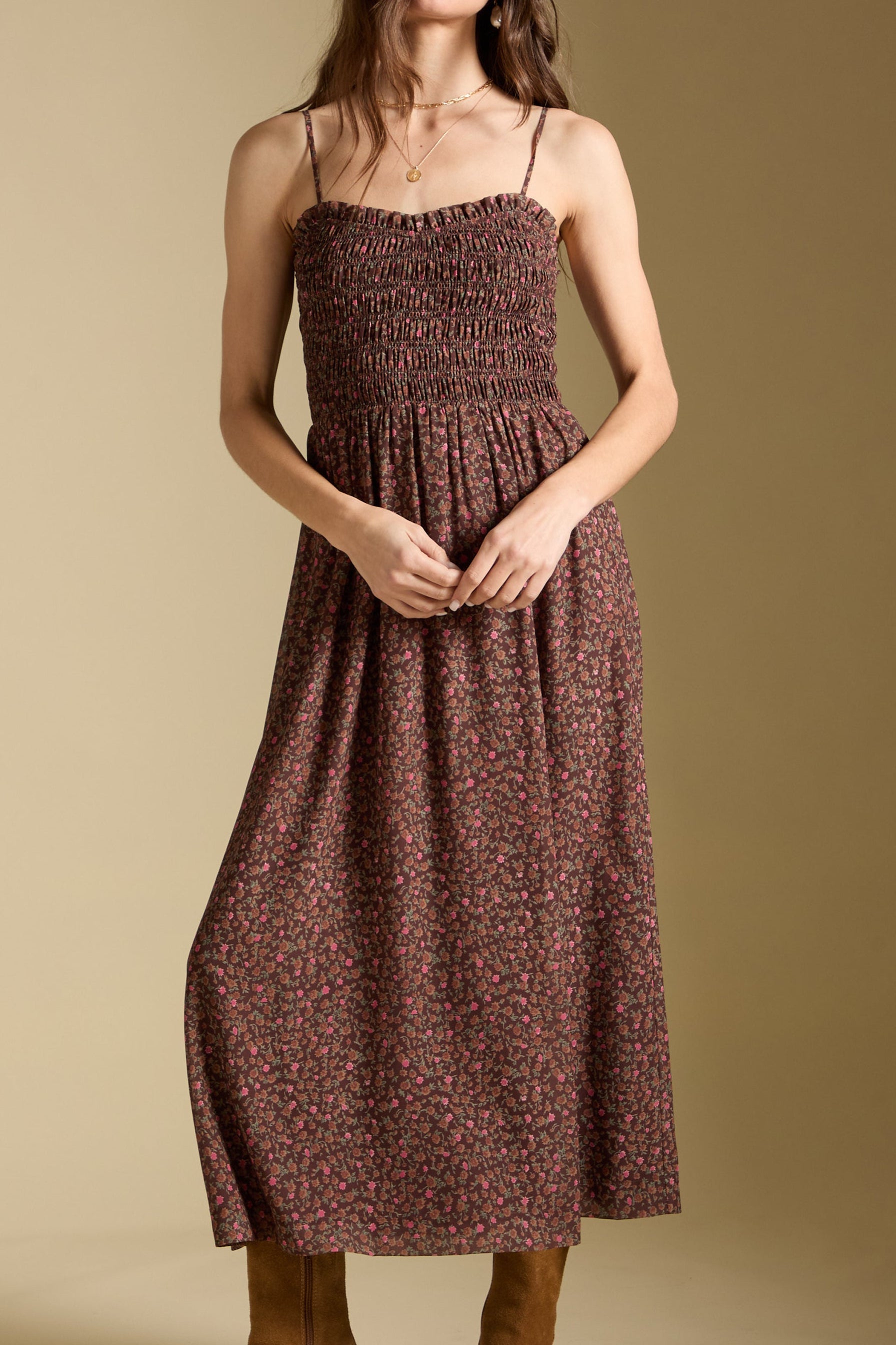 Woman wearing a patterned dress, white hat, and brown boots against a beige background
