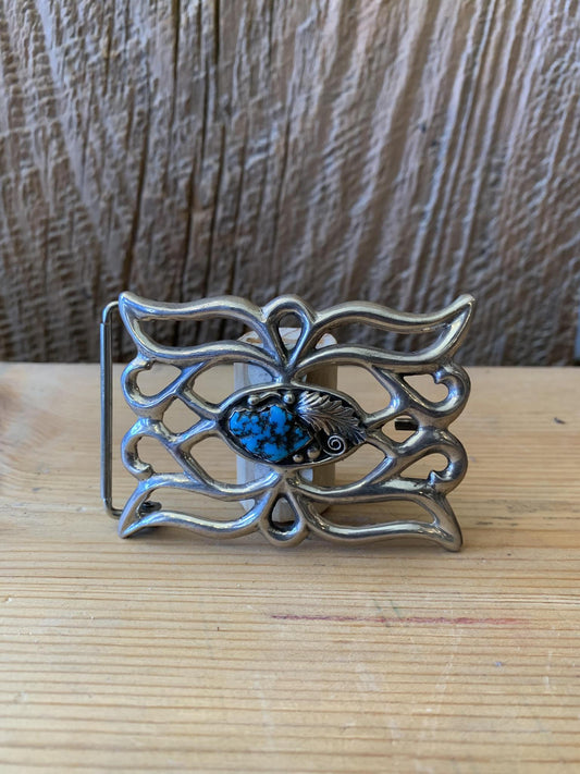 A vintage sterling silver belt buckle with turquoise detailing and a central blue stone, set against a wooden background.