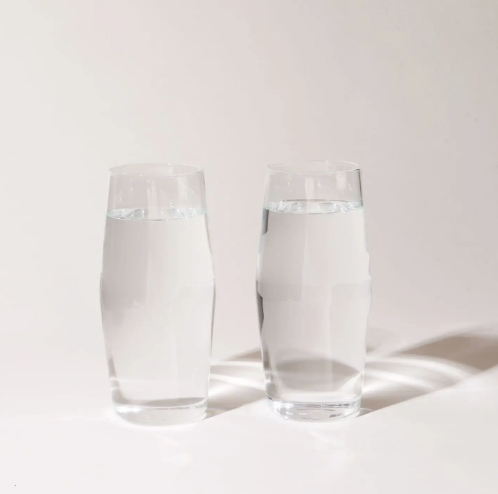 Two clear glass highball glasses with water on a white background.