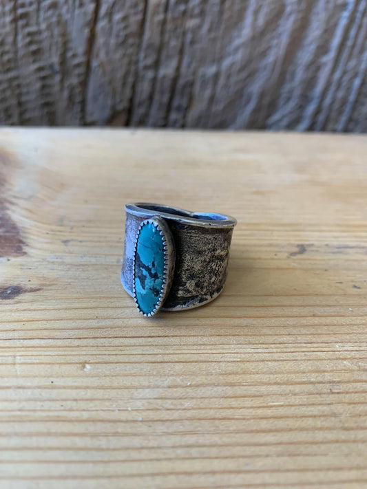 A hand forged sterling silver ring with a turquoise talon design on a wooden surface.
